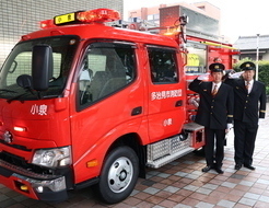 [写真]小泉消防団の2人が配属車両の前で敬礼する様子